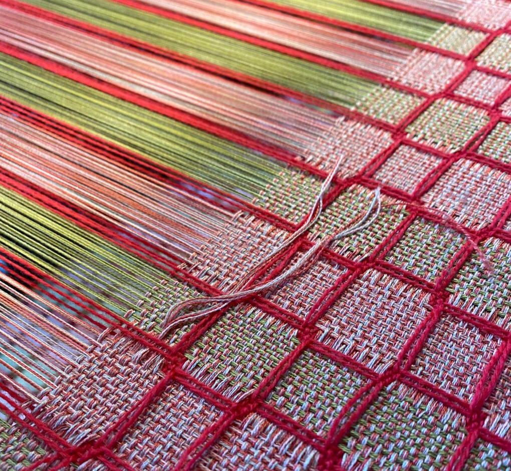 Work-in-progress shot of a handwoven green, red, and pink scarf on the loom